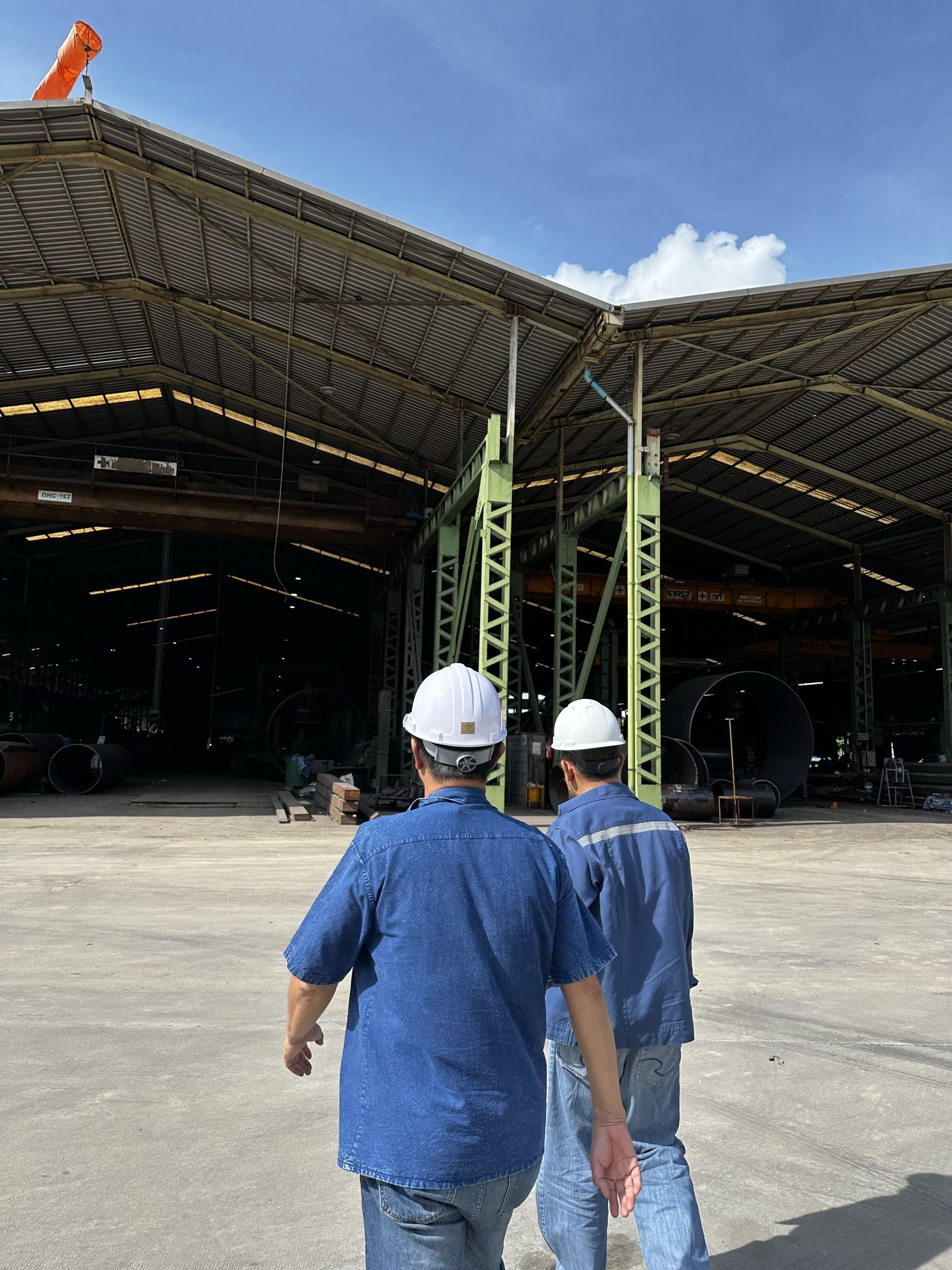 Engineers walking through the fabrication workshop past rolled steel cylinders